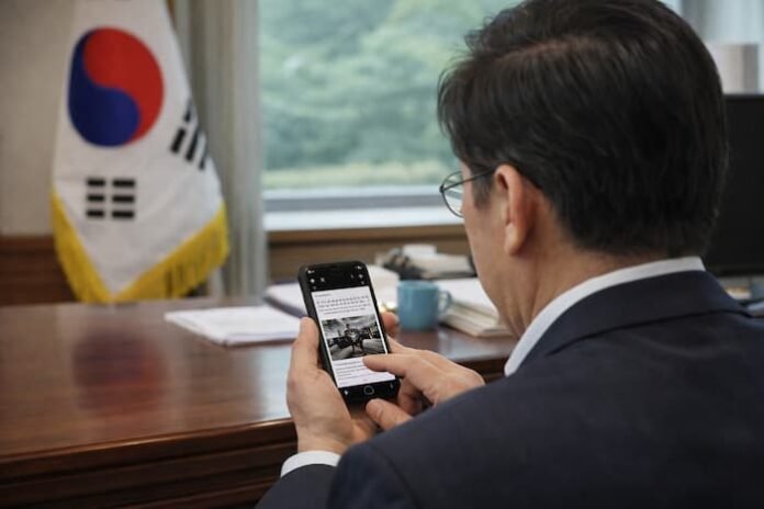 책상 위에서 스마트폰을 확인하는 중년 남성의 모습과 배경의 태극기