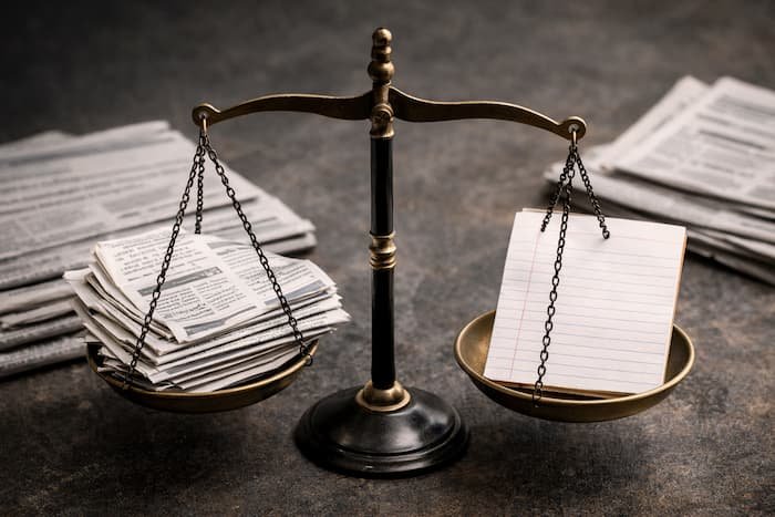 저울 위 기사 문서와 빈 메모지가 놓여 균형 상실을 상징하는 언론 비평 이미지